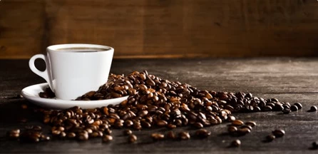 Warto mielić kawę samemu. Świeżo zmielone ziarna zachowują swój smak i aromat. Filiżanka kawy w otoczeniu ziaren kawowca.